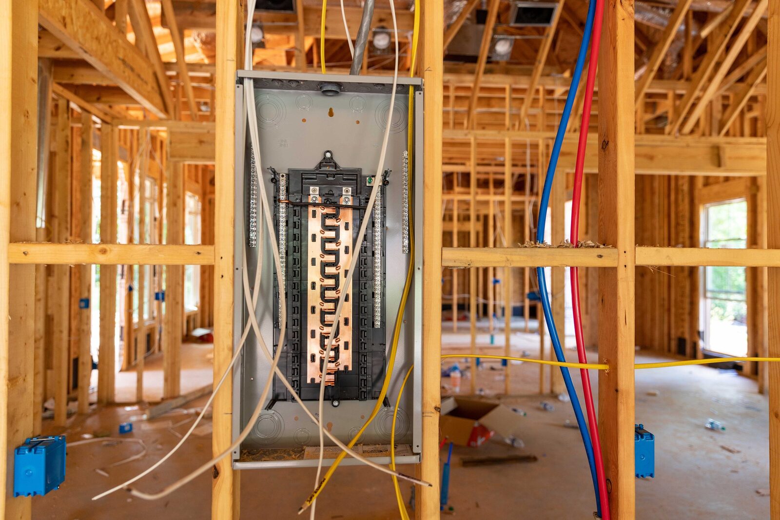 Electrical panel installed in the wooden framing of a house under construction, with colorful wires connected to it.