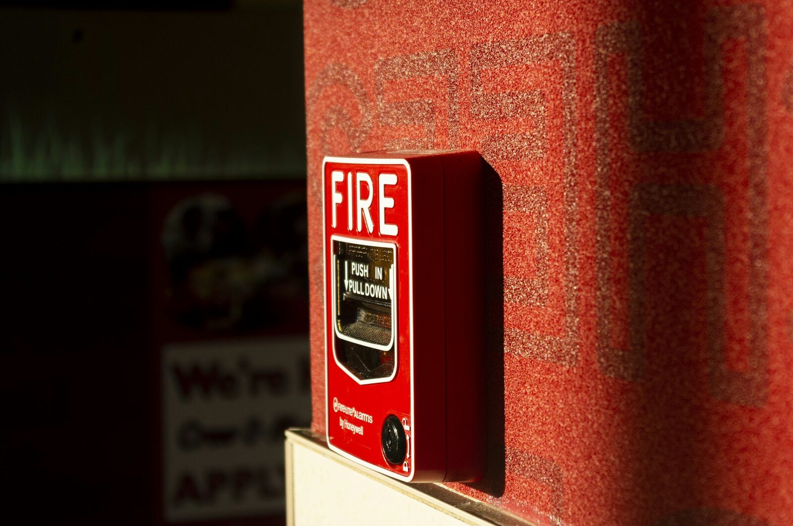 Red fire alarm pull station mounted on a textured red wall.