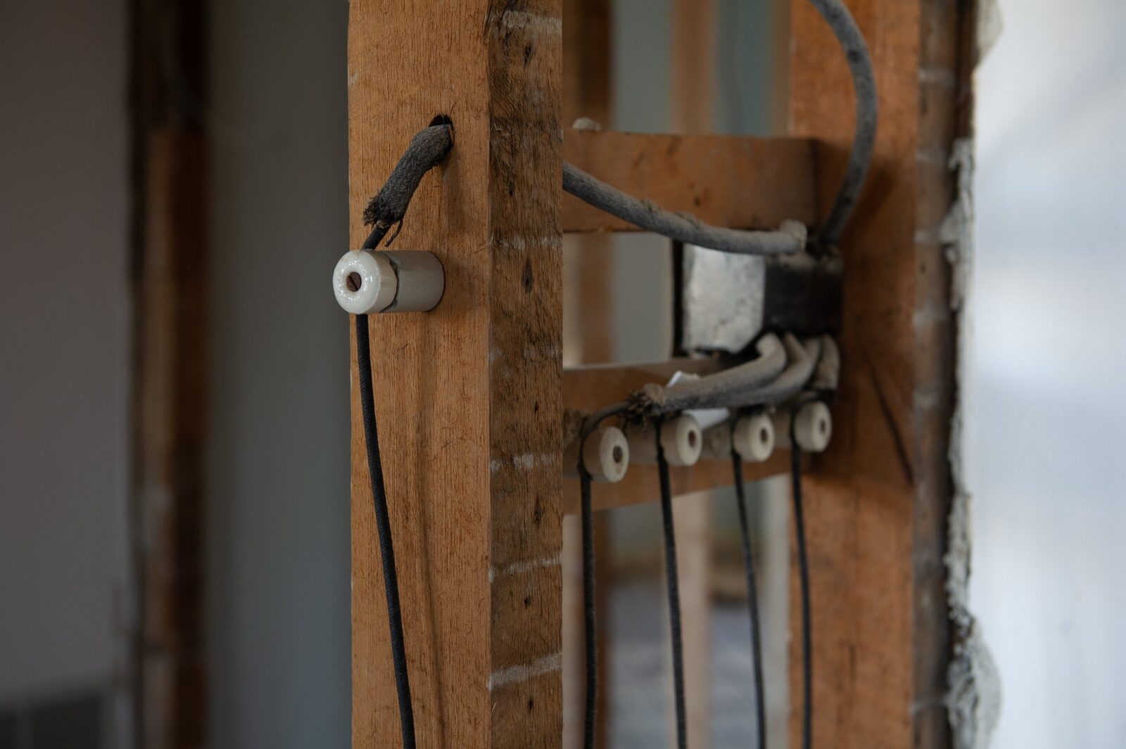Close-up of a wooden wall with electrical wires and ceramic insulators mounted, showing an unfinished electrical installation.