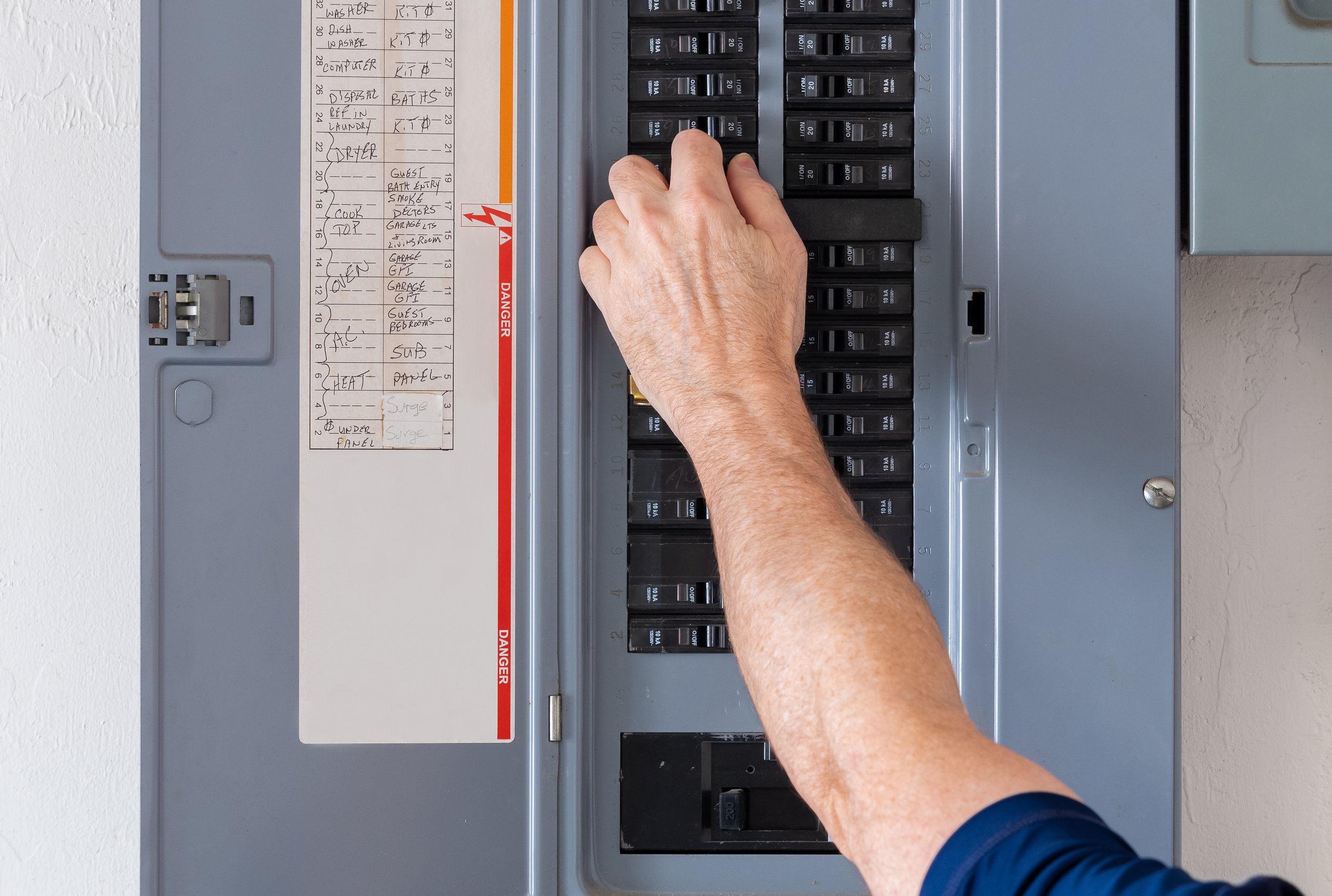 A person flipping a circuit breaker in an electrical panel with a list of labels on the side.