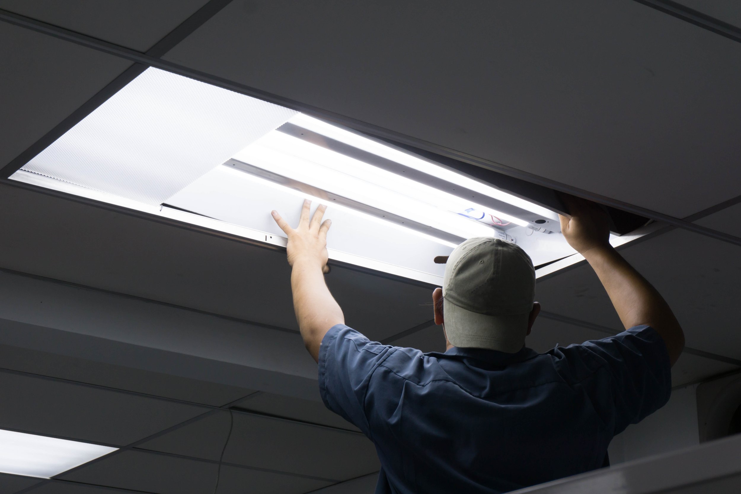 Electrician working on a fluorescent troffer fixture in an office drop ceiling